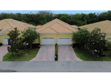 Charming two-unit villa featuring a yellow exterior, tile roof, and brick-paved driveway leading to attached garages at 4837 Rainbow Race, New Port Richey, FL 34652