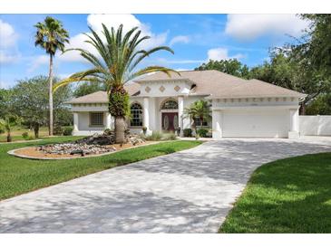 Elegant exterior with lush landscaping, palm trees, water feature, and a paver driveway to a two-car garage at 18644 Autumn Lake Blvd, Hudson, FL 34667