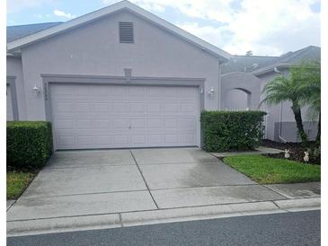 Beige home showcasing a two-car garage, complimented by lush landscaping and concrete driveway at 20720 Eustis Rd, Land O Lakes, FL 34637