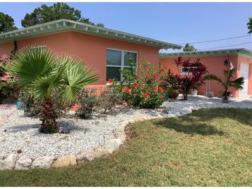 Charming home features a colorful landscaped front yard with vibrant flowers and a small palm tree at 406 Driftwood E Dr, Palm Harbor, FL 34683