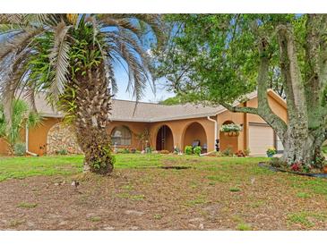Inviting single-story home featuring a meticulously manicured lawn, mature trees, and an arched entryway at 4190 Lema Dr, Spring Hill, FL 34609