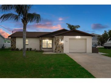 Charming single-story home featuring a well-maintained lawn and a classic stone facade detail at sunset at 7520 Mako Dr, Hudson, FL 34667