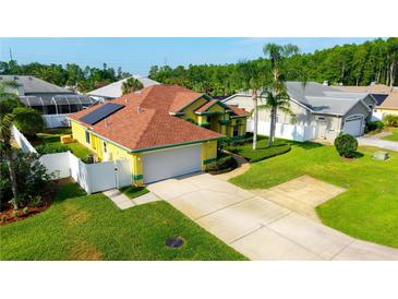 Inviting yellow two-car garage home featuring a red-tile roof, solar panels, and a well-manicured lawn at 21820 Carson Dr, Land O Lakes, FL 34639