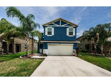 Two-story blue home featuring a large two-car garage, well-manicured lawn, and beautiful palm trees at 14008 Lugano Ct, Hudson, FL 34669