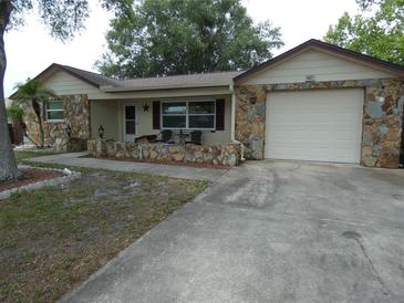 Charming home with a rock facade, attached garage, and inviting front porch with chairs and table at 7421 Fairfax Dr, Port Richey, FL 34668