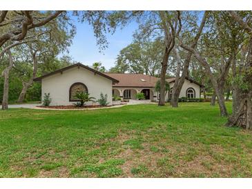 Charming home featuring a well-manicured lawn, a circular driveway, and a unique architectural design at 4595 Lake In The Woods Dr, Spring Hill, FL 34607