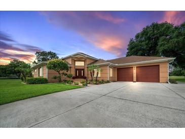 Exterior view of home featuring a brick facade, a two-car garage, well-maintained lawn, and dusk sky at 10044 Twelve Oaks Ct, Spring Hill, FL 34613