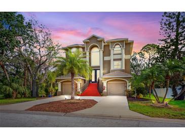 Stunning custom home with red stairs, mature landscaping, and a grand entrance at dusk at 7340 Brightwaters Ct, New Port Richey, FL 34652