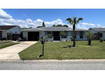 Charming home featuring an inviting front yard with lush greenery and a palm tree, creating a tropical ambiance at 7534 Briarwood Dr, Port Richey, FL 34668