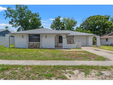 Charming single-story home featuring stone accents, a gray roof, and mature trees in a suburban neighborhood at 16018 Adobe Dr, Hudson, FL 34667
