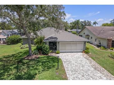 Charming home featuring a two-car garage, brick-paved driveway, and mature landscaping at 2486 Deer Trail Ln, Spring Hill, FL 34606