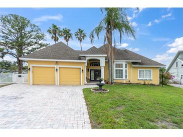 Charming yellow home with a two-car garage, brick driveway, manicured lawn, and mature palm trees at 5440 Manatee Point Drive, New Port Richey, FL 34652