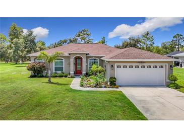 Charming home showcasing a well-manicured lawn, complemented by a red front door and a two-car garage at 12323 House Finch, Weeki Wachee, FL 34614