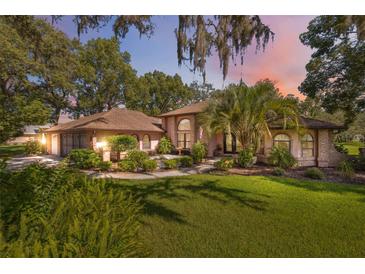 Inviting exterior with a well-manicured lawn and lush landscaping surrounding the pink stucco and brick home at 12295 Clarendon Ct, Spring Hill, FL 34609