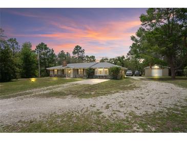Charming single-story home with a spacious driveway, detached garage and metal roof surrounded by lush landscaping at 13345 Convent Garden Rd, Brooksville, FL 34613
