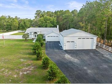 Stunning single Gathering home with attached and detached garages, lush lawn, and white perimeter fence at 15430 Oakcrest Cir, Brooksville, FL 34604