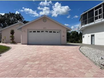 A well-maintained pink house with a two-car garage and a patterned brick driveway under a blue sky at 20971 Negril Ct, Lutz, FL 33558