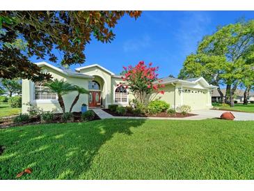 Charming single-story home featuring a well-manicured lawn, lush landscaping, and a welcoming entrance with red doors at 14178 Pullman Dr, Spring Hill, FL 34609