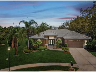 Inviting exterior showcasing a beautifully landscaped yard, tiled roof, and attached two-car garage at 5903 Cachette De Riviera Ct, New Port Richey, FL 34655