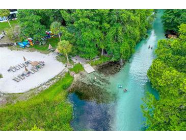 A scenic aerial view shows a sandy beach with lounge chairs and a clear, flowing river perfect for swimming at 6462 River Run Blvd, Weeki Wachee, FL 34607
