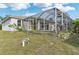 View of the home's exterior featuring a screened in patio, yard with grass, and a bright blue sky above at 2781 Shady Ave, North Port, FL 34286