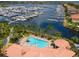 Aerial view of a kidney-shaped community pool, surrounded by palm trees and lounge chairs with a marina in the background at 611 Riviera Dunes Way # 308, Palmetto, FL 34221