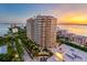 An aerial view showcases a luxury high-rise building, tropical landscaping, and waterfront views at sunset at 35 Watergate Dr # 503, Sarasota, FL 34236