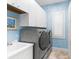 Neat laundry room with blue wallpaper, white cabinets, a window, and modern washer/dryer units at 757 Hideaway Bay Dr, Longboat Key, FL 34228