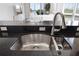 Close-up of a stainless steel kitchen sink with a modern faucet and dark countertop, offering a glimpse of the living area at 611 Riviera Dunes Way # 108, Palmetto, FL 34221