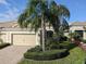 Charming home featuring a paved driveway, two-car garage, tropical landscaping with palm trees and lush green grass at 4830 Maymont Park Cir, Bradenton, FL 34203