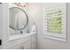 Small bathroom with white vanity, round mirror, and plantation shutters at 4013 Red Rock Ln, Sarasota, FL 34231