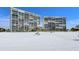 Exterior view of two beachfront condo buildings with white sand beach and clear blue sky at 19 Whispering Sands Dr # 204, Sarasota, FL 34242