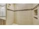 Beige tiled shower with mosaic trim and built-in shelving at 7546 Divot Loop, Lakewood Ranch, FL 34202