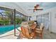 Covered patio with a wooden dining set, ceiling fan, and view of lush greenery and the sparkling pool at 218 Brandywine Circle, Englewood, FL 34223