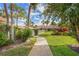 Paved walkway leading to community buildings featuring tropical plants, a manicured lawn, and bright blue sky at 3375 Sandleheath # 34, Sarasota, FL 34235