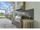 Outdoor kitchen featuring a grill, beverage cooler, and sink, all under a screened lanai with beautiful backyard views at 8332 Sea Glass Ct, Sarasota, FL 34240