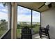 View from the screened-in balcony with black railings and chairs overlooking lush greenery, lake, and palm trees at 1010 Tidewater Shores Loop # 201, Bradenton, FL 34208