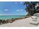 White sand beach with turquoise water, rocks, lounge chairs, and covered seating area at 1249 S Basin Ln, Sarasota, FL 34242