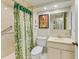 Bathroom featuring a shower with green curtain, toilet, decorative wall art, and cream colored cabinets at 1102 Benjamin Franklin Dr # 407, Sarasota, FL 34236