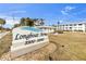 Community sign for Longboat Arms with manicured grass, tropical palms, and blue sky at 3320 Gulf Of Mexico Drive # 208C, Longboat Key, FL 34228