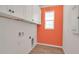 Laundry room with white cabinets, orange accent wall, and wood-look tile floor at 4151 Via Sienna Cir, Sarasota, FL 34243