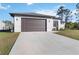 Concrete driveway leading to a two-car garage with brown door, landscaping, and white exterior walls at 1256 Napoleon Rd, North Port, FL 34288