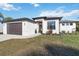 Modern single-story residence with a two-car garage, dark roof, white exterior, and green lawn at 1256 Napoleon Rd, North Port, FL 34288