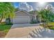 The front of the home features a two-car garage, lush landscaping, and a welcoming walkway at 114 Fieldstone Dr, Venice, FL 34292