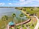 An aerial view displays a scenic lakefront with a boardwalk, palm trees, and residential community at 8412 Whispering Woods Ct, Lakewood Ranch, FL 34202