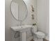 Bathroom with a white pedestal sink, round mirror, modern light fixture, and tiled floor at 8328 Sea Glass Ct, Sarasota, FL 34240