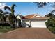 Charming single-story home featuring a brick driveway, white garage doors, tropical landscaping, and a red tile roof at 9203 Winter Harbour Way, Bradenton, FL 34212