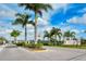Community entrance featuring tropical palm trees and lush landscaping under a clear blue sky at 7668 Registrar Way, Sarasota, FL 34243