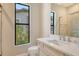 Bathroom boasts stone countertop, white cabinets, and tiled shower with glass door and window at 10612 Nicklaus Ct, Englewood, FL 34223
