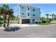 Beautiful three-story coastal home with a light blue facade, complemented by a two-car garage, and lush palm trees at 630 Companion Way, Longboat Key, FL 34228